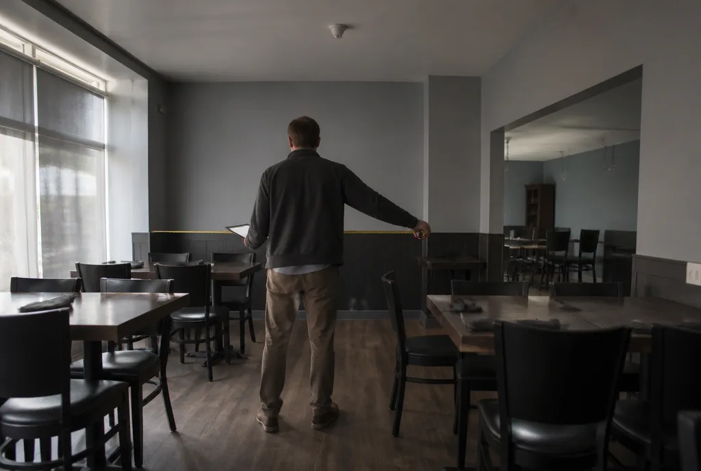 An inspector seen from behind pulling a tape measure across the aisle of a finished restaurant dining room